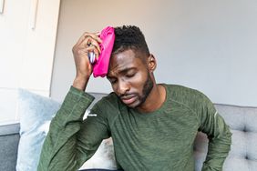Man holds a pink ice pack to his head - stock photo