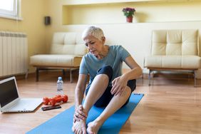 Senior woman sitting on a yoga mat, grabbing an ankle
