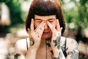 A woman sitting outdoors massaging the bags under her eyes