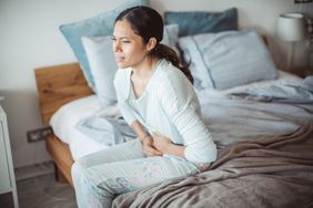 person with biliary dyskinesia experiencing abdominal pain while sitting on bed 