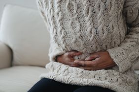 Close-up of a black woman sitting on sofa holding her abdomen in pain, feeling bloated