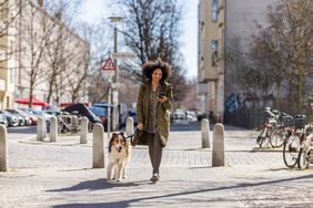A young woman texting on her phone while walking her dog