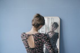A narcissistic young woman in vintage dress looking into mirror