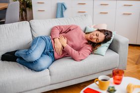 woman laying down on her couch having stomach pain 