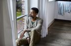 older man sitting on the floor looking sad while staring out the window 