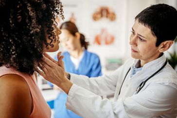 Female doctor examining a female patient in his medical office while female nurse writing information about patient
