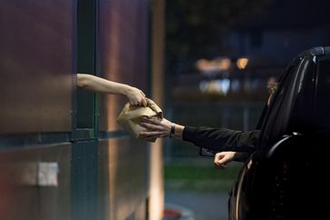 A fast food employee hands a bagged meal to someone in their car through the drive-thru window
