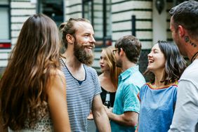 A young group of friends meeting together at a barbecue are chatting and smiling as they greet each other.