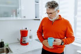 A man with constipation holding a cup of coffee in the kitchen