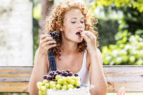 female eating grapes with bowl of grapes in foreground
