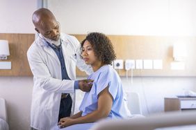 Male doctor treating female patient sitting in hospital gown on bed
