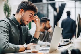 tired man sitting at desk experiencing symptoms of b12 deficiency
