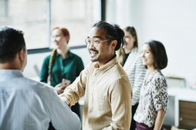 Asian man wearing glasses and a yellow button down shakes hands with a colleague