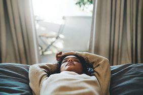 female laying on bed with arms above her head eyes closed