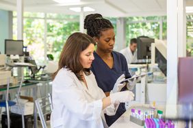 Close-up of female pathologist and technician using digital tablet while organizing samples in test tube rack for processing in Argentine clinical analysis lab.