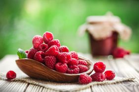 Fresh forest raspberries in wooden basket on rustic table. Sweet raspberry jam in background.