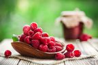 Fresh forest raspberries in wooden basket on rustic table. Sweet raspberry jam in background.