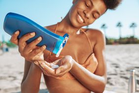 person putting sunscreen in hand sitting on a beach