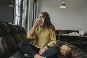 Female sneezing into a tissue sitting on a couch