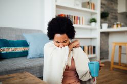woman coughing into her elbow holding a cup of tea