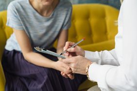 A woman sits on the couch as a female doctor writes on a clipboard