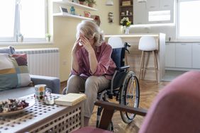 female in wheelchair with hands on forehead in living room