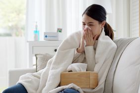 Female sitting on couch under a blanket blowing her nose