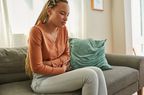 woman sitting on couch holding stomach in pain