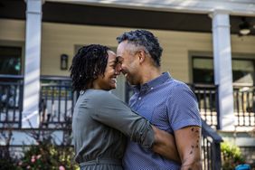 Couple holding each other close and smiling in front of a house