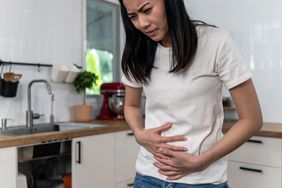 Young woman experiencing gallstone pain while standing in the kitchen at home.