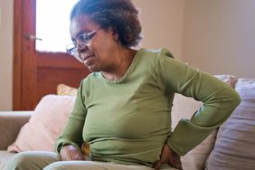 Senior woman having backache sitting at home. Elderly female is suffering from pain. She is wearing casuals.