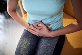 White female clutching stomach sitting on edge of couch