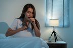Female sitting in bed coughing with hand on chest and in front of mouth