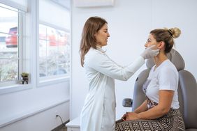 White female doctor examining White female patient's face