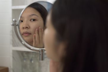 person checking face for mole in the mirror