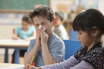 little boy blowing his nose in a classroom because of influenza symptoms