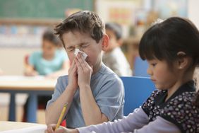 little boy blowing his nose in a classroom because of influenza symptoms