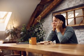 Young depressed woman sitting at dining table during breakfast and thinking of something.