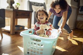 Older sister gives younger happy brother a ride in the laundry basket