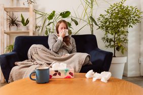 Sick woman sitting on the couch and blowing her nose and drinks hot drink