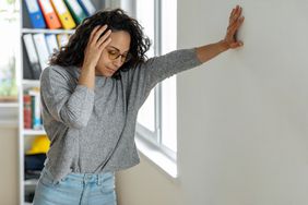 Woman leaning against wall with dizziness and difficulty standing up