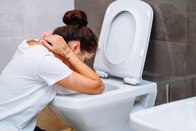 Woman with hair bun holding her neck by hands, sit in kneeling pose in bathroom