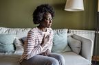 Woman sitting on couch feeling chest pain and difficulty breathing