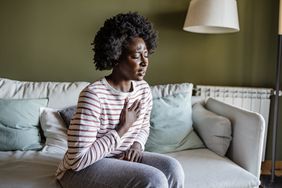 Woman sitting on couch feeling chest pain and difficulty breathing