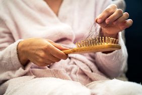 Woman in a pink bathrobe pulling hair out of a brush. 