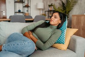 Young woman lying on the sofa clutching stomach