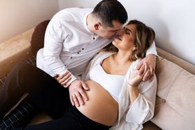 Pregant female and male kissing on couch with male's hand on pregnant belly