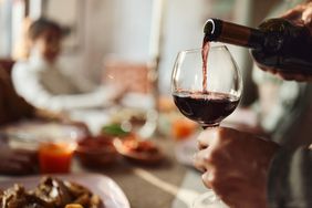 Wine being poured from bottle into glass in foreground; person in background out of focus
