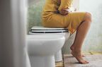 Woman in a yellow dress sitting on top of a toilet clutching her stomach