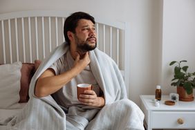 Man sitting in bed rubbing throat